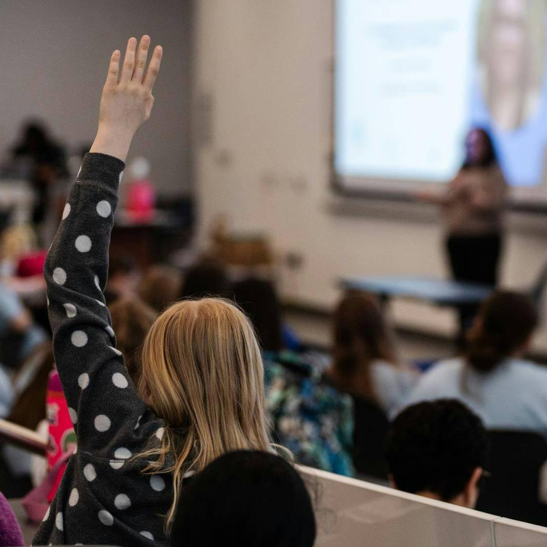 A young girl raises her hand to ask a question during a presentation in an auditorium.