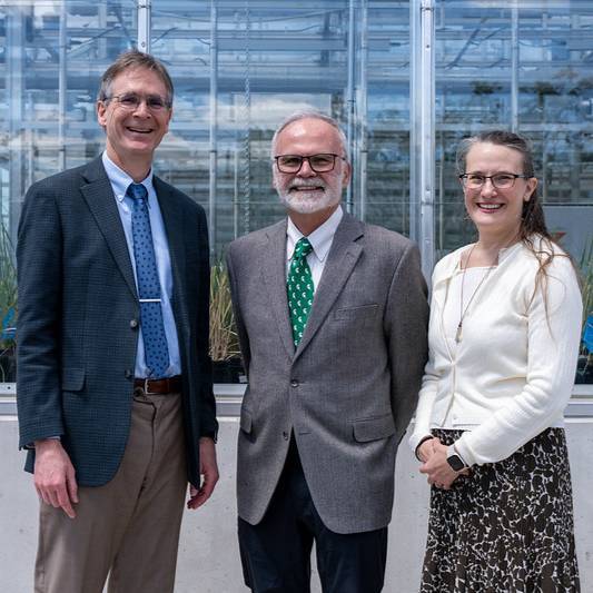 Three people stand outside of a greenhouse smiling