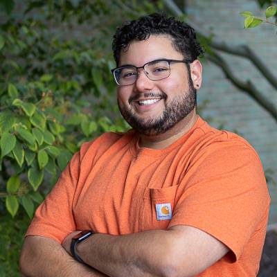A headshot of Kevin Santiago‑Morales in an orange shirt taken outside