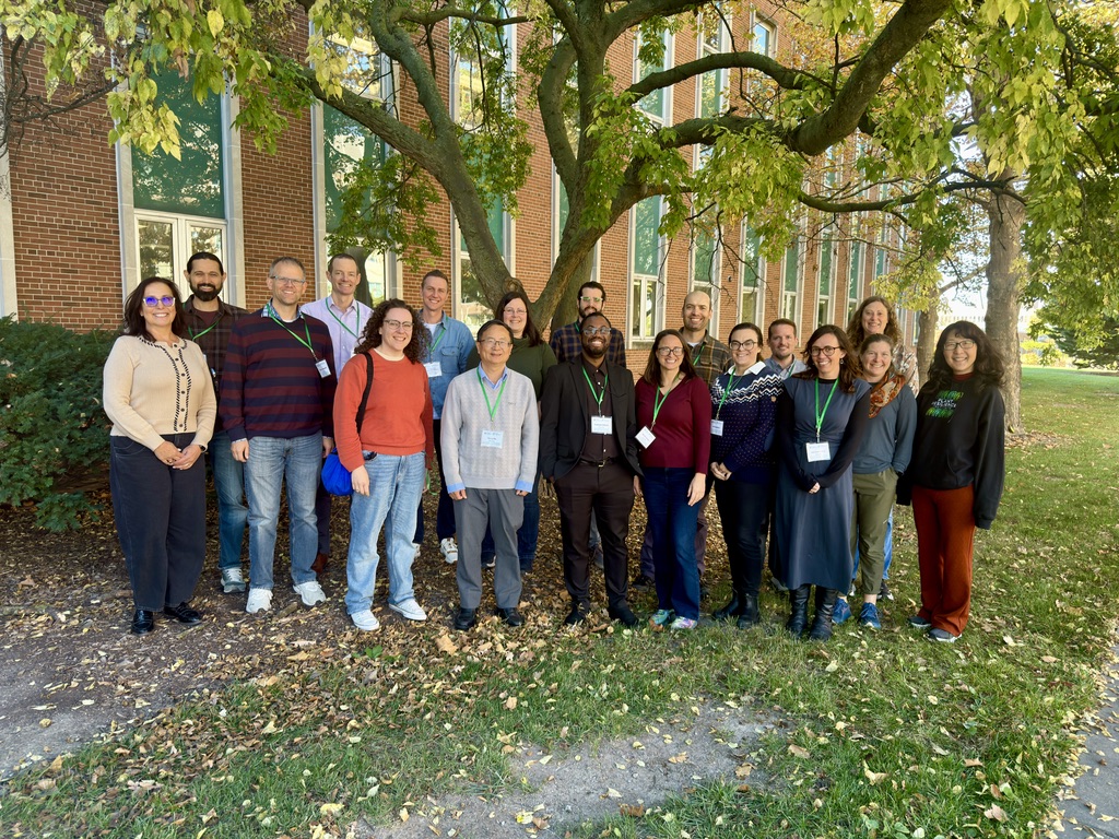 A group photo of 18 people standing together outside in front of a tree