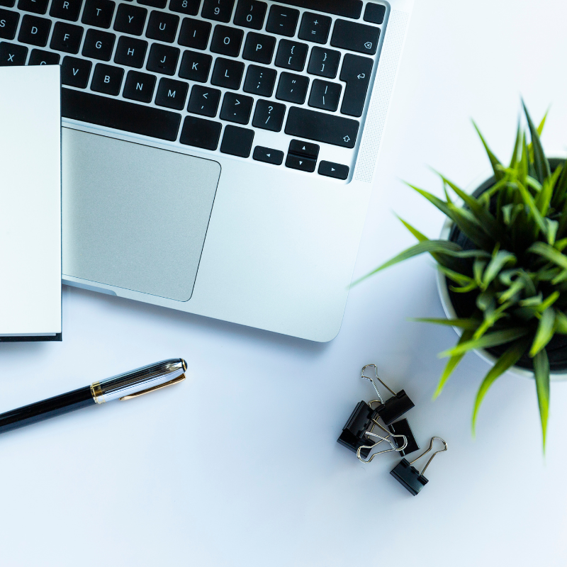 A laptop, various office supplies, and a small potted plant pictured top-down on a table