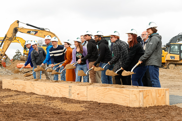A dozen people wearing Spartan hard hats and holding shovels at the Plant and Environmental Sciences Building groundbreaking ceremony with excavators in the background.