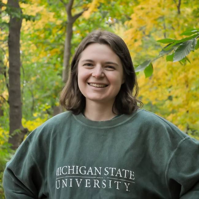 A headshot of Rachel Drobnak pictured wearing an MSU sweatshirt outside in front of autumn leaves