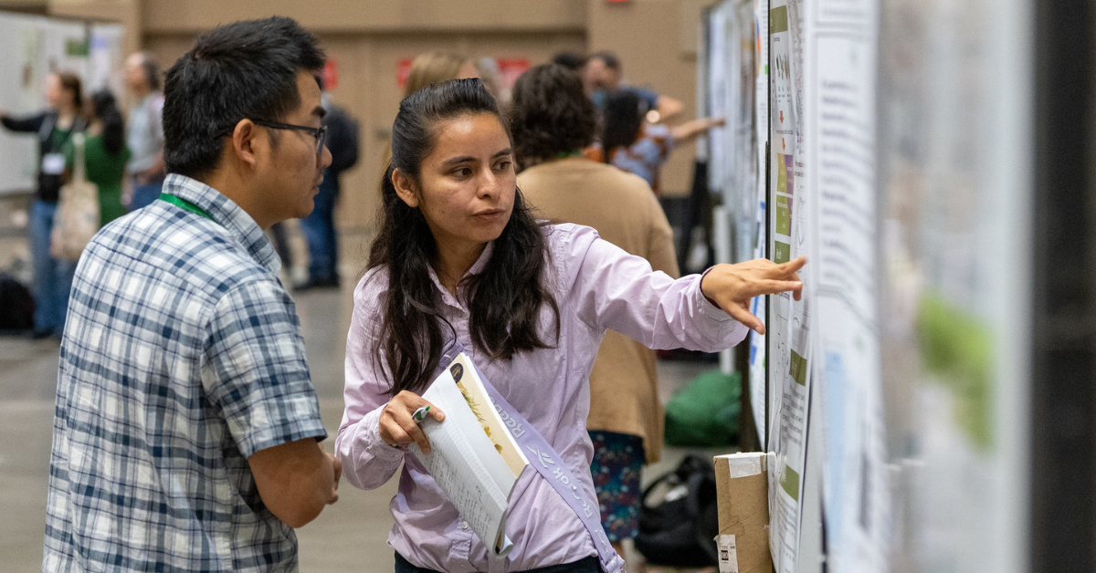 A woman points to a research poster while holding a book as a man looks at where she's pointing